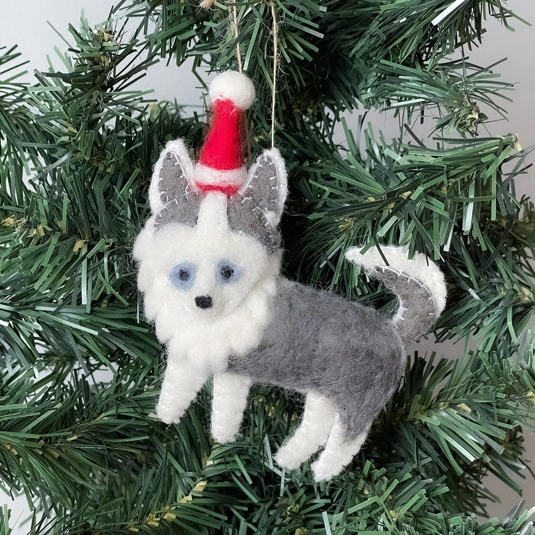 Felt dog ornament with a red Santa hat hanging on a Christmas tree.