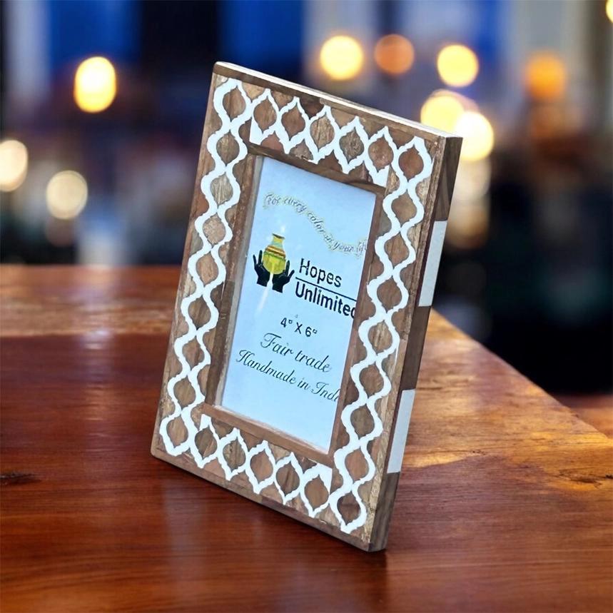 Wooden photo frame with decorative white lattice design on a wooden surface with blurred lights in the background.
