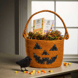 Wicker basket with Halloween decorations including a black cat and pumpkins on a table.