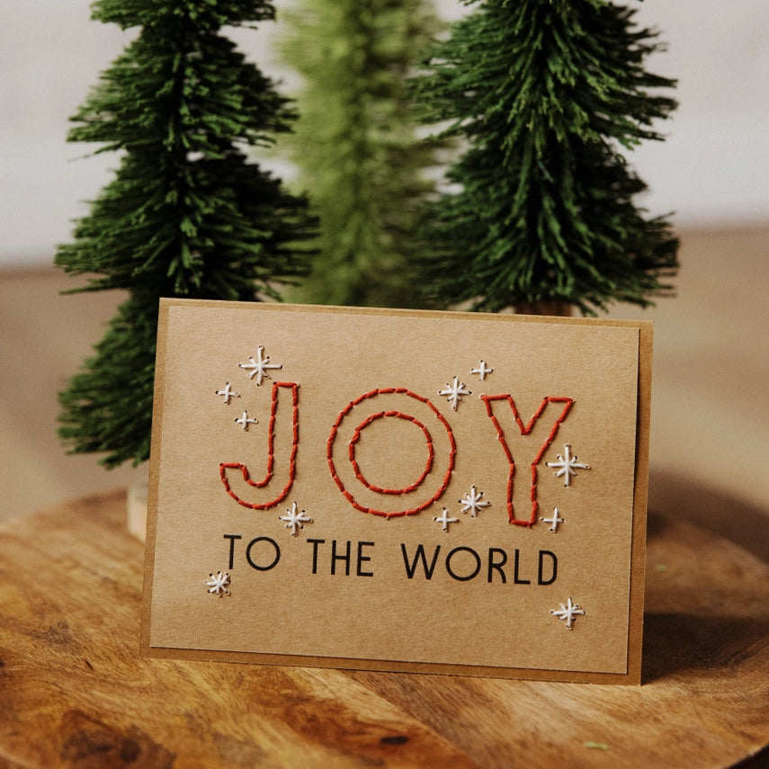 Card with 'Joy to the World' text in front of small Christmas trees