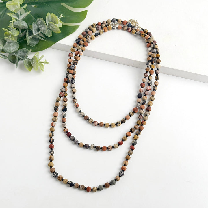 Multicolored beaded Kantha necklace on a white surface with green leaves in the corner