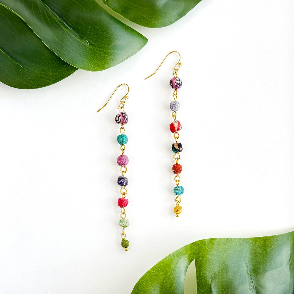Kantha Colorful beaded earrings on a white background with green leaves.