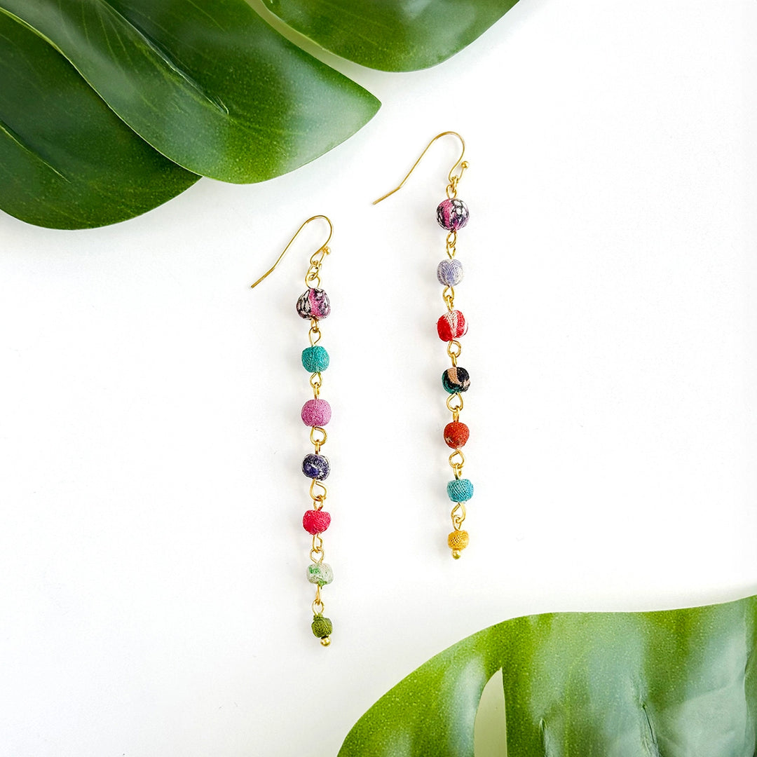 Kantha Colorful beaded earrings on a white background with green leaves.