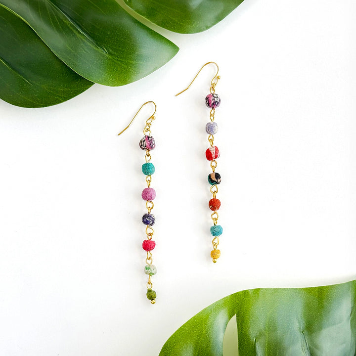 Kantha Colorful beaded earrings on a white background with green leaves.