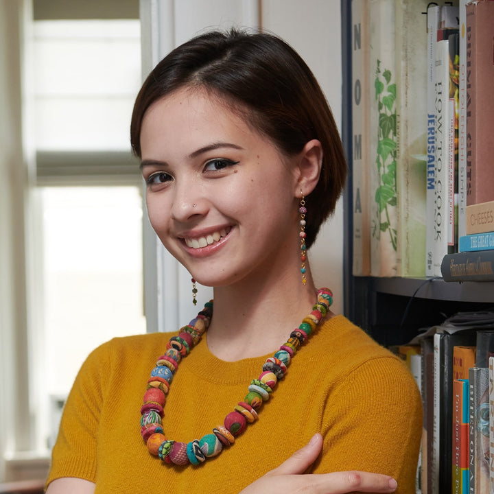 Woman wearing a colorful Kantha linear dangle earrings in a room with books on shelves