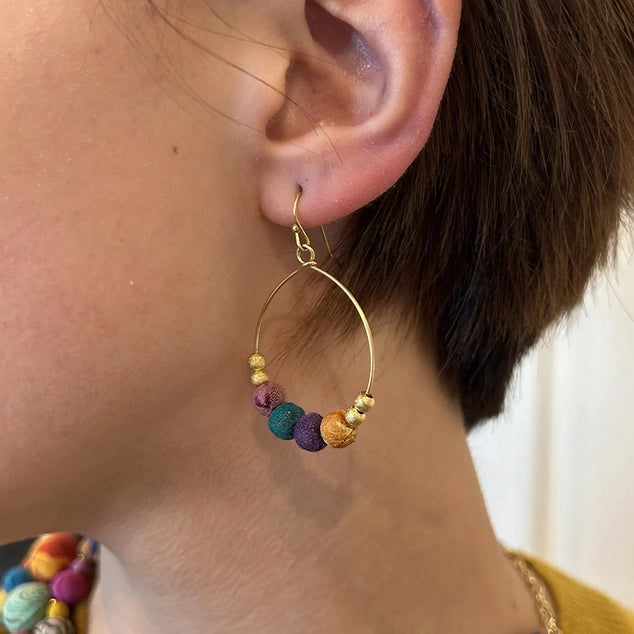 Close-up of gold hoop earring with colorful beads worn by a person.