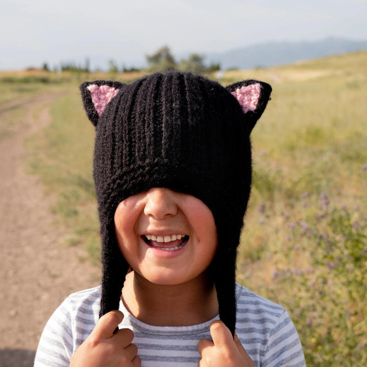 Child wearing a black knitted hat with cat ears in an outdoor setting