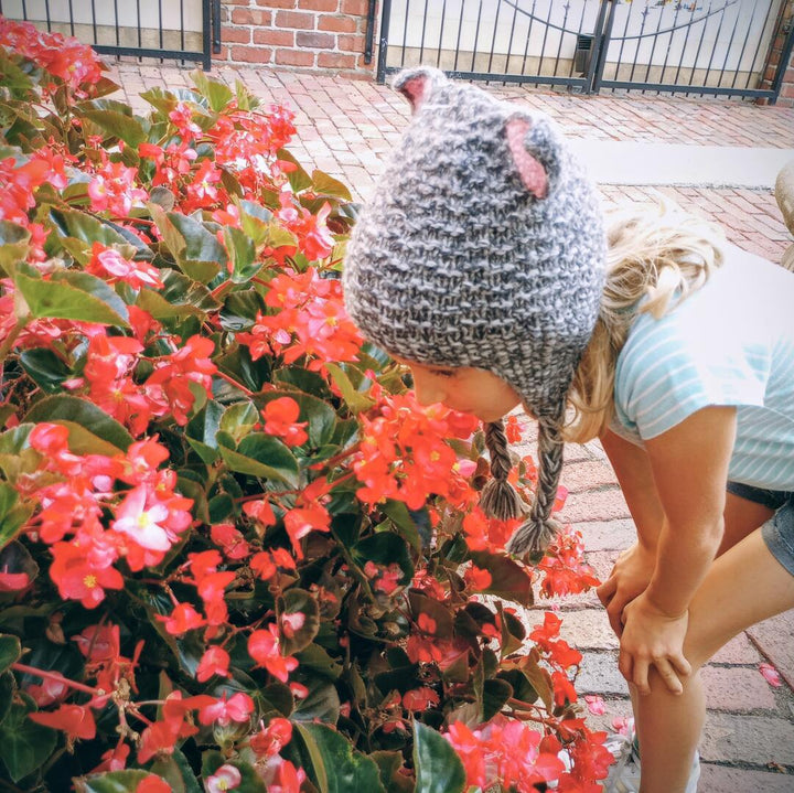 Person wearing a knitted hat interacting with red flowers on a brick path
