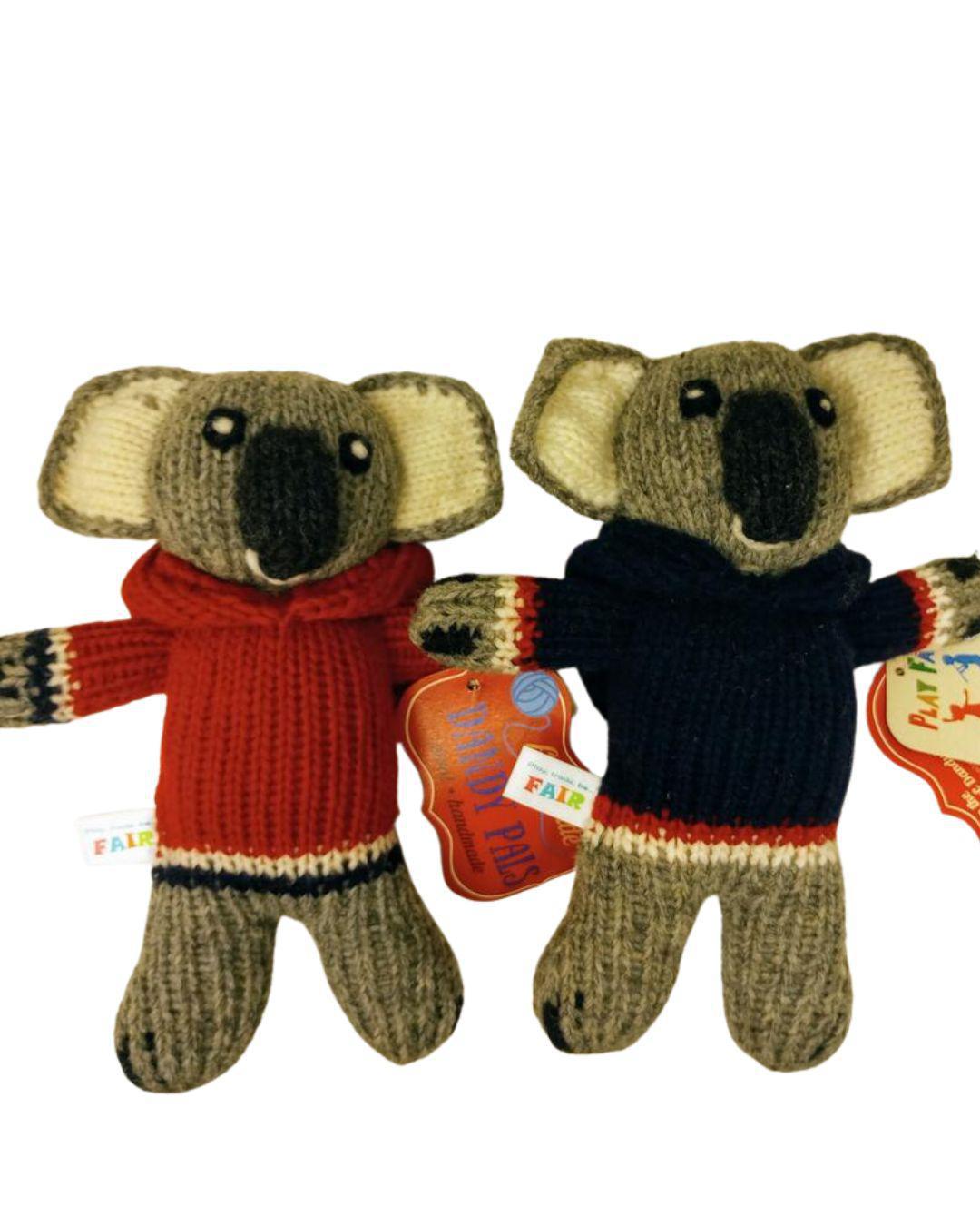 Two knitted koala toys wearing sweaters with visible tags on a white background