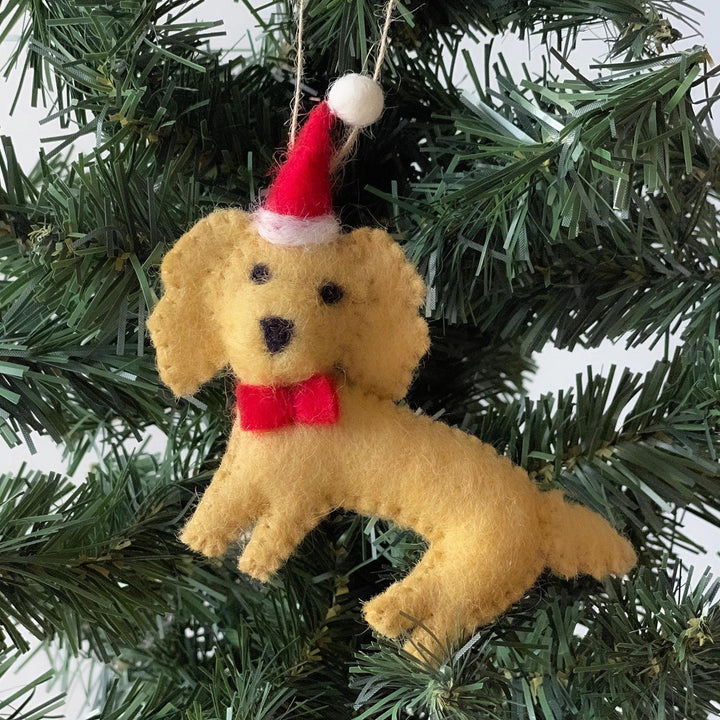 Dog-shaped Christmas ornament with a Santa hat and red bow tie hanging on a tree.
