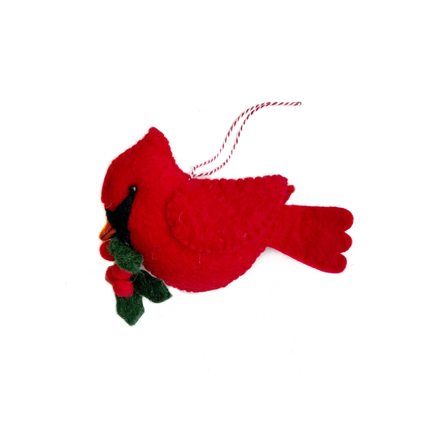 A red felt cardinal Christmas ornament holding green holly leaves and red berries, with a red and white striped hanging string, shown on a plain white background.
