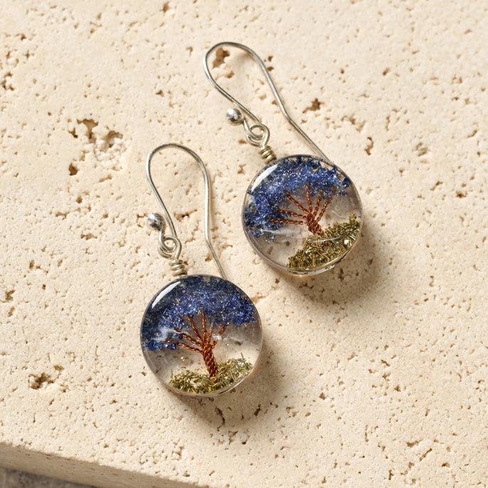 Pair of earrings with nature-themed tree design on a beige surface