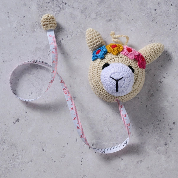 Crocheted llama measuring tape  on a concrete surface