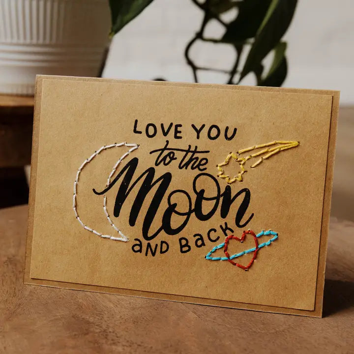 Kraft paper card with 'Love you to the moon and back' text and embroidered design on a wooden surface.