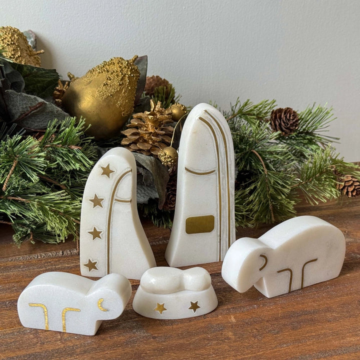 Decorative nativity set with white figures and gold accents on a wooden surface with Christmas decorations.