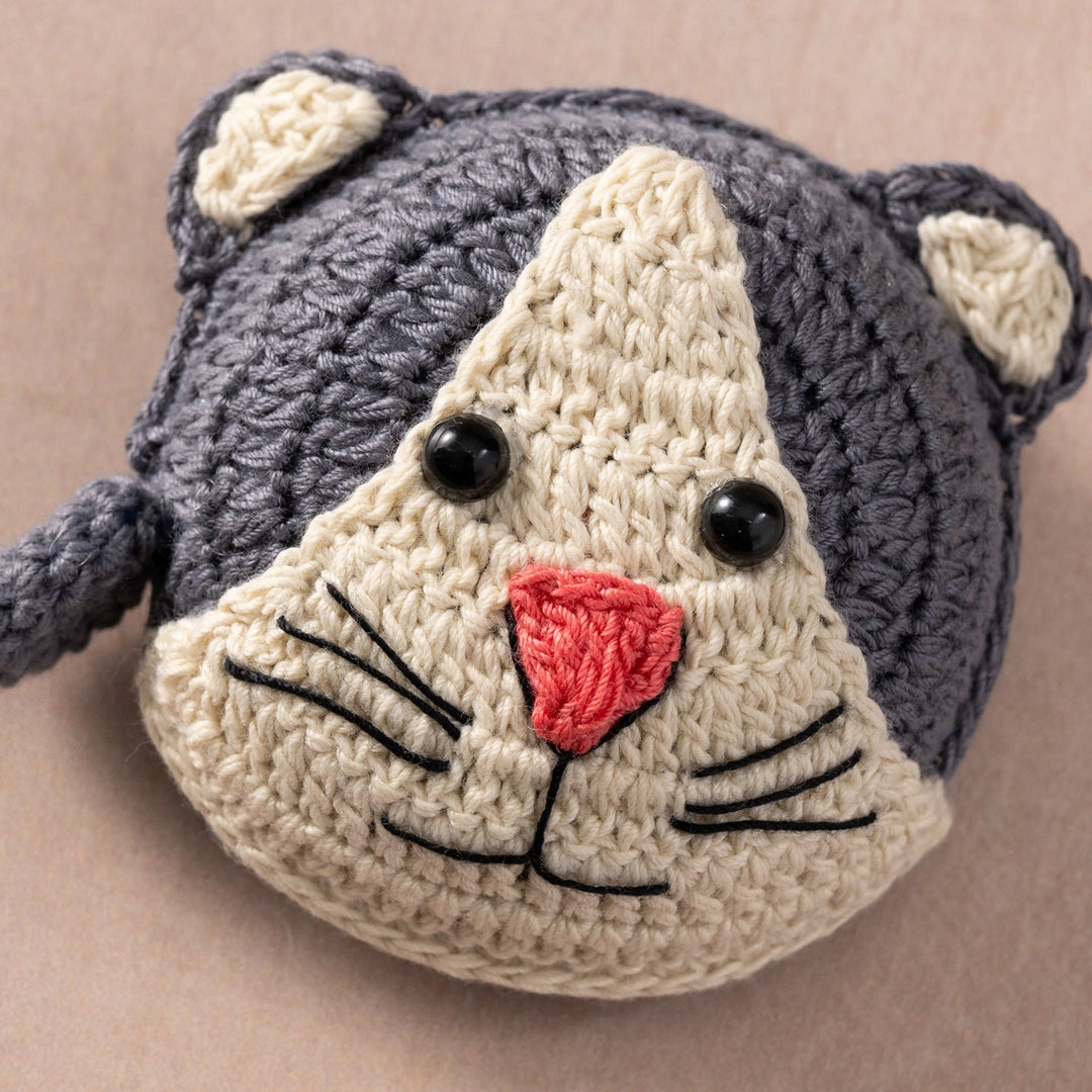 Crocheted cat measuring tape with gray body and beige face on a beige background