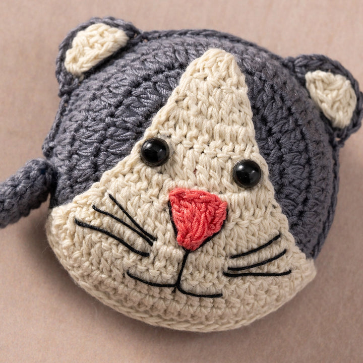 Crocheted cat measuring tape with gray body and beige face on a beige background