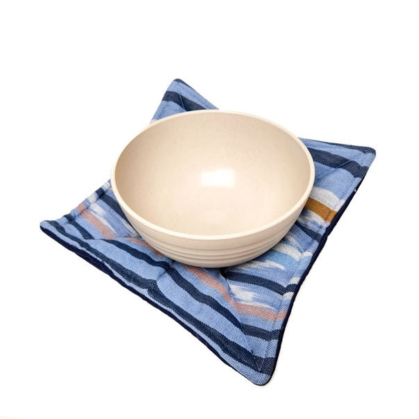 Beige ceramic bowl on a blue bowl cozy against a white background