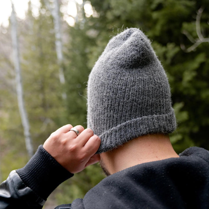 Person wearing a gray knit beanie with a forest in the background