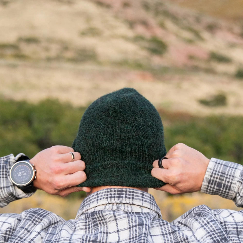 Person wearing a green beanie with a blurred natural landscape in the background