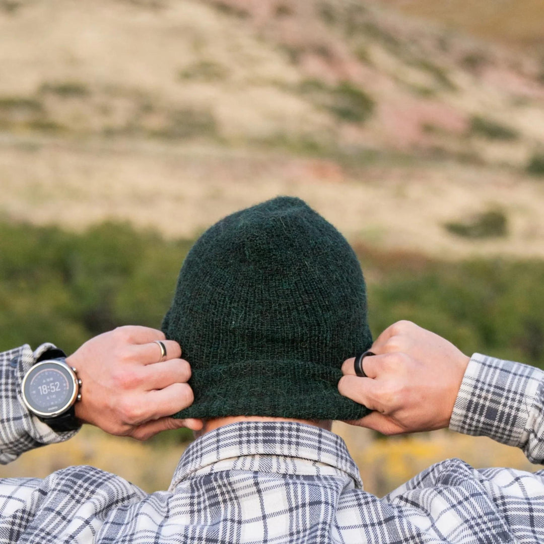 Person wearing a green beanie with a blurred natural landscape in the background