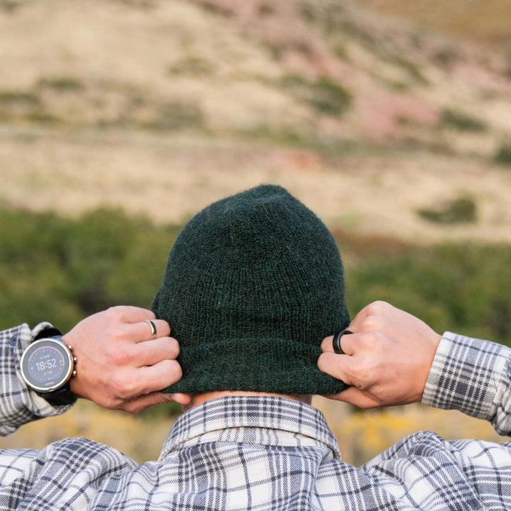 Person wearing a green beanie with a blurred natural landscape in the background