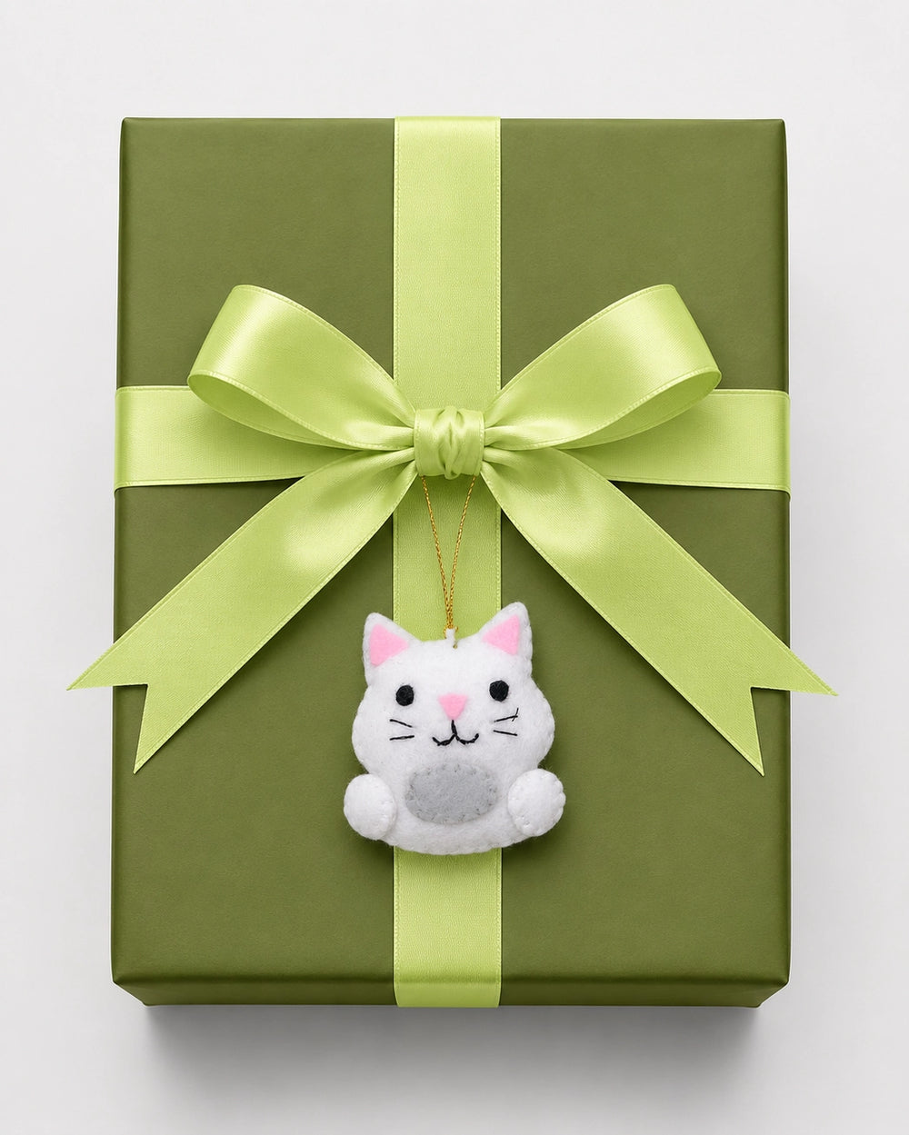 Green gift box with a large green bow and a small white cat ornament on a light gray background
