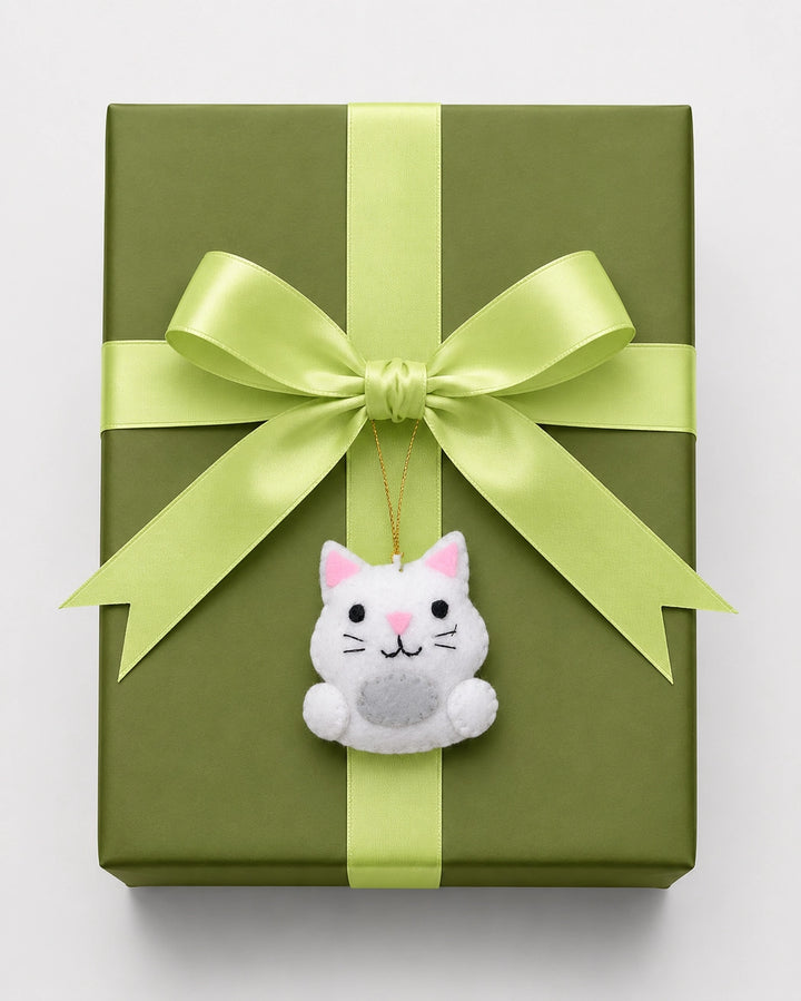 Green gift box with a large green bow and a small white cat ornament on a light gray background