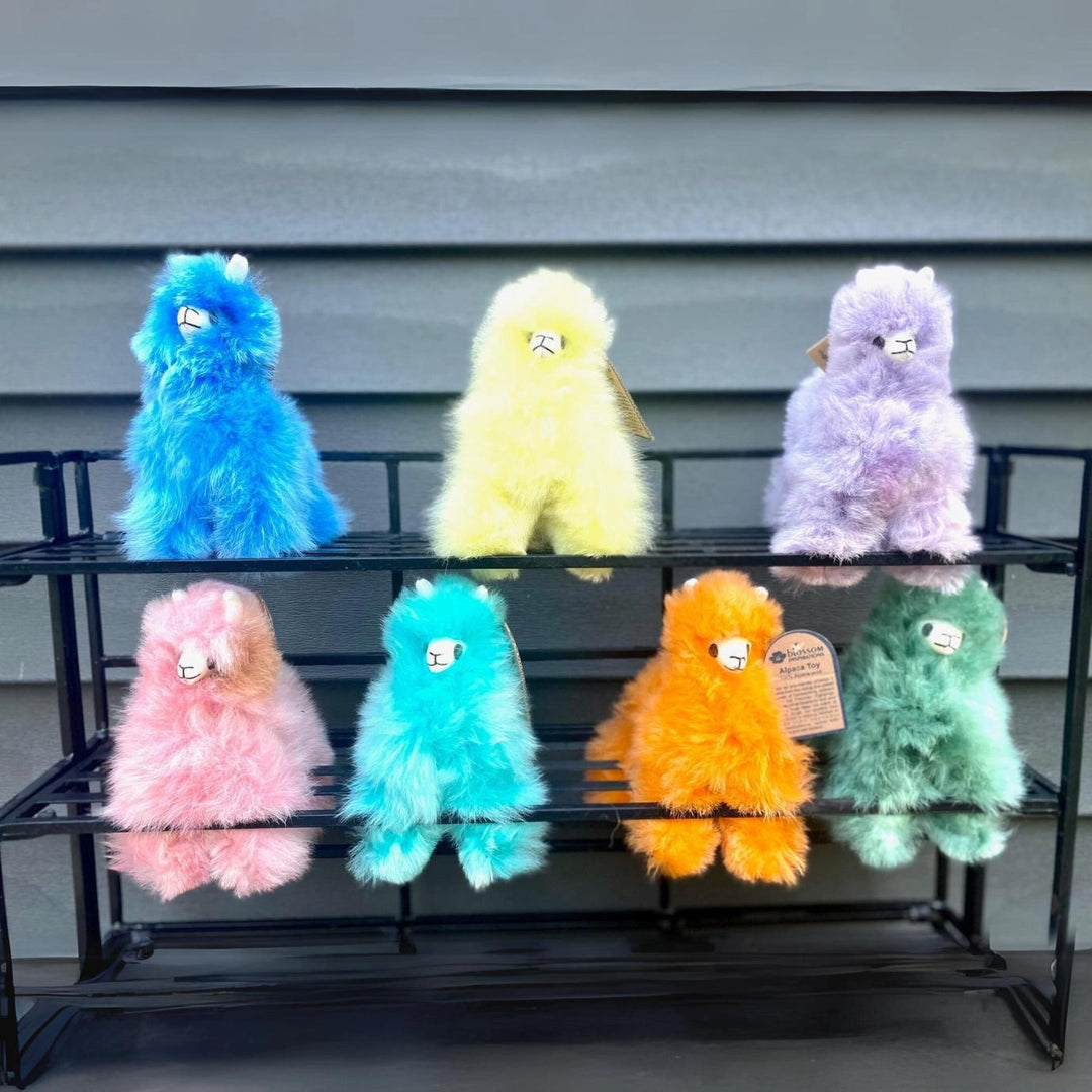 Colorful fluffy alpaca figurines on a black metal shelf against a gray wall.