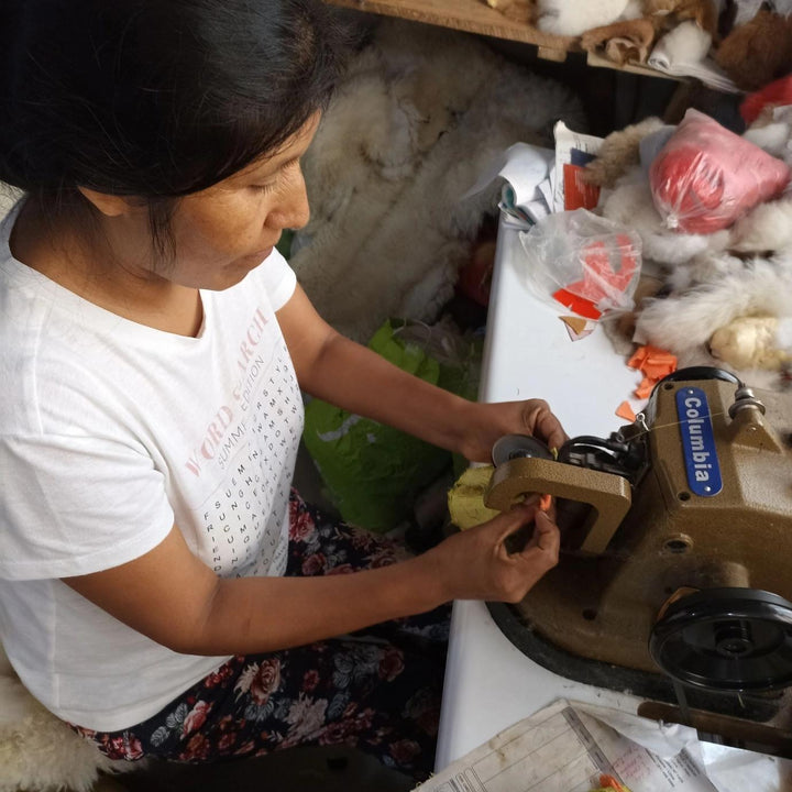 Woman operating a machine to make the alpaca figurines, fur in background.