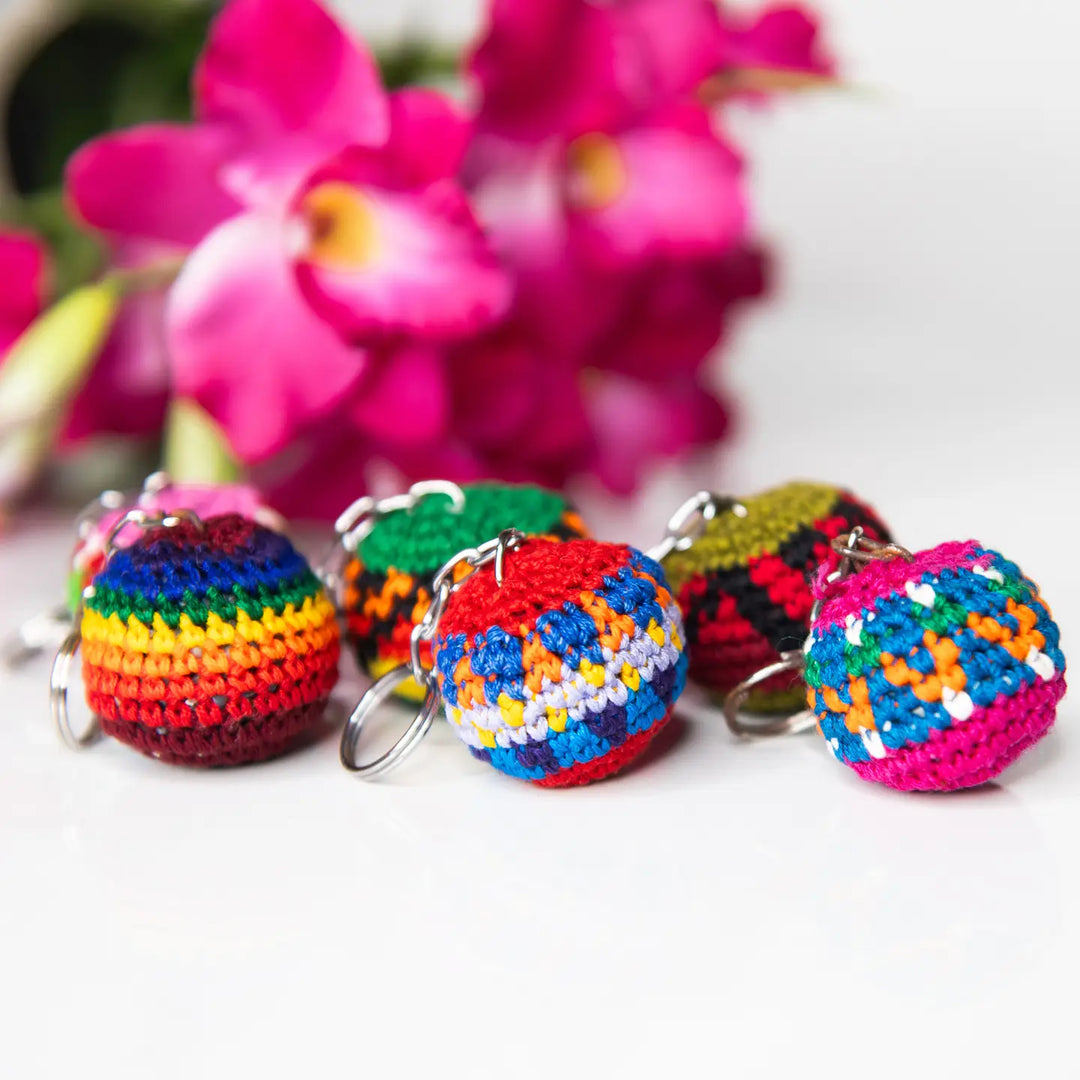 Colorful crocheted keychains on a white surface with pink flowers in the background
