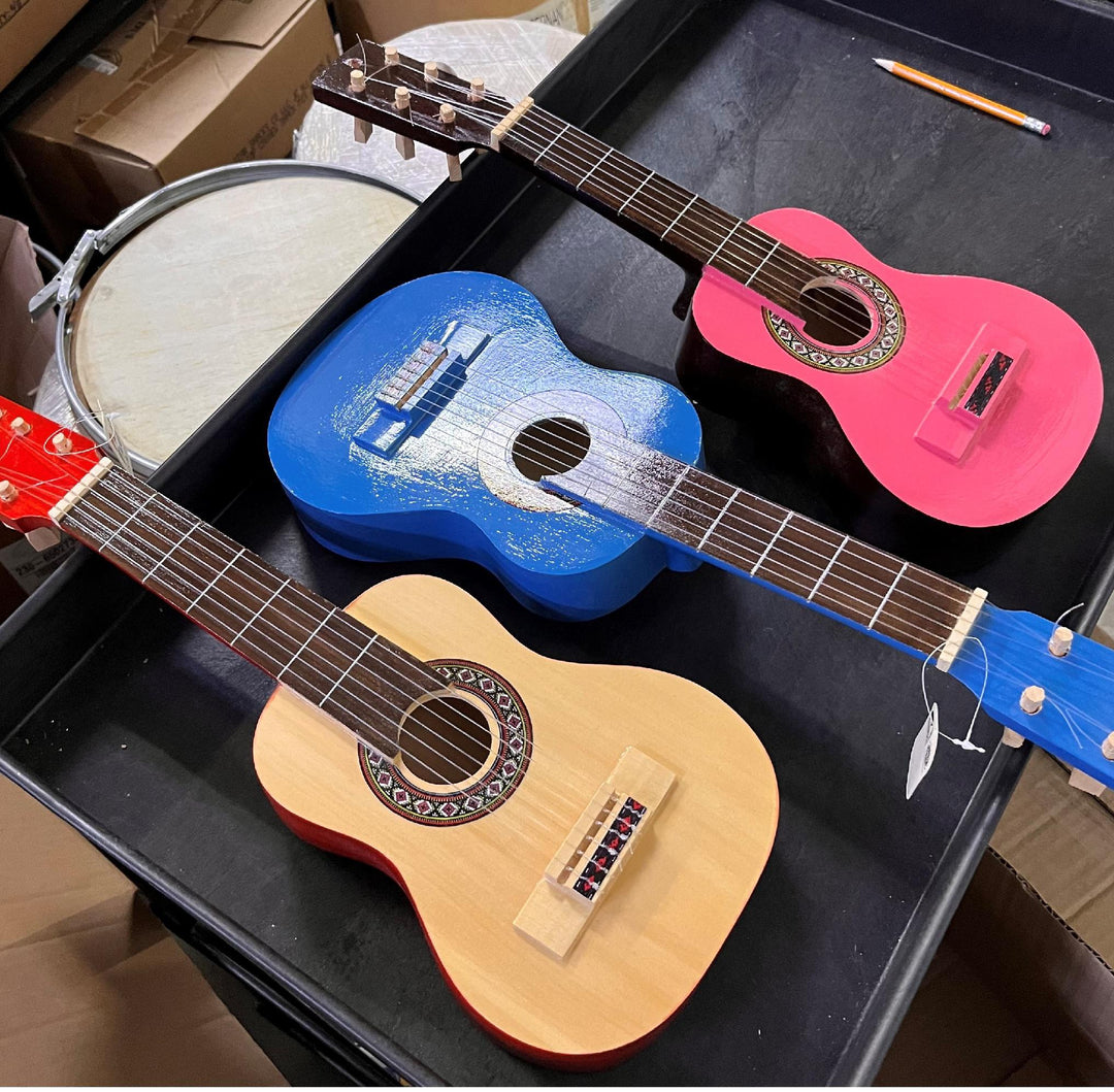 Three mini guitars in blue, pink, and red colors, displayed on a flat surface, with a wooden body and plastic strings.