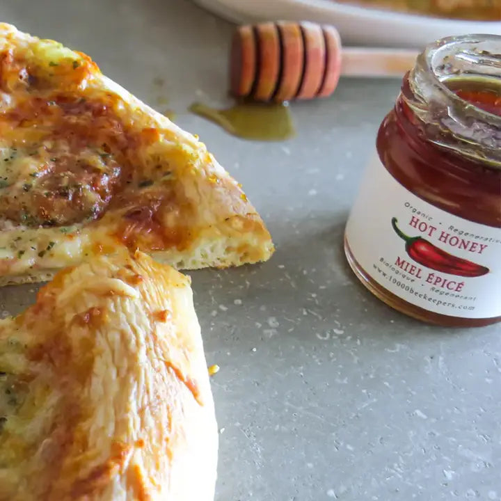 pizza slice next to jar of mini hot honey with a honey dipper