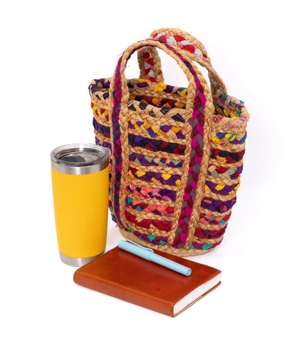 Colorful braided bag with a yellow tumbler and brown notebook on a white background