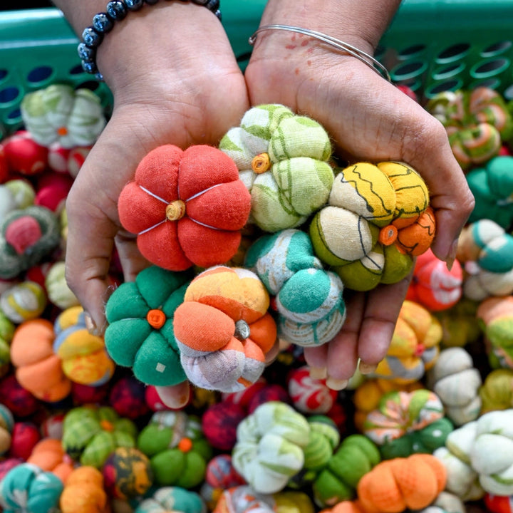 Colorful fabric pumpkins held by a person with a basket of more pumpkins in the background.