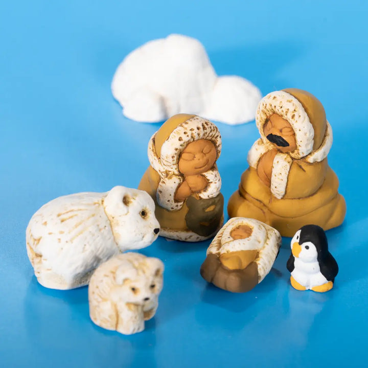 A set of small figurines on a bright blue background, including two polar bear figures, two arctic-style human figures in tan and cream clothing, a small brown-and-white animal figure, and a black-and-white penguin figure.