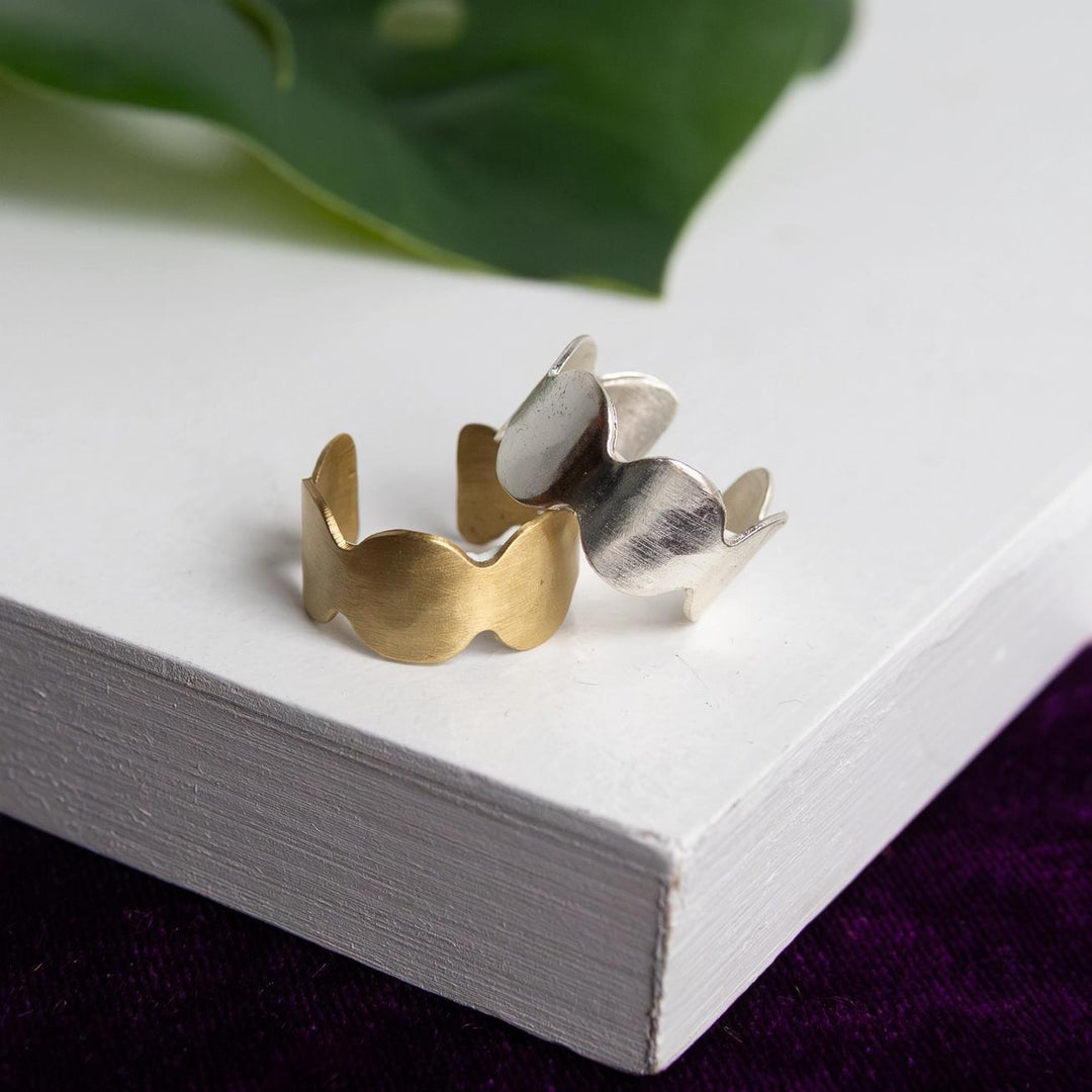 Gold and silver ring on a white surface with green leaves in the background
