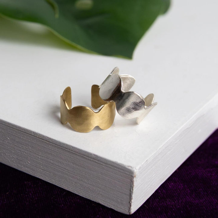 Gold and silver ring on a white surface with green leaves in the background