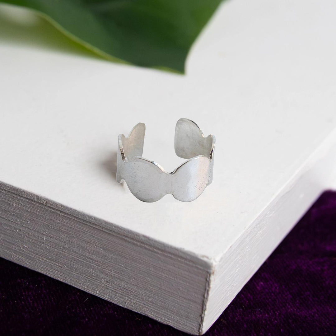 Silver ring on a white surface with green leaves in the background