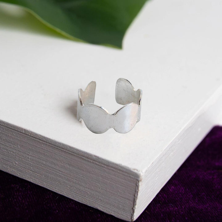 Silver ring on a white surface with green leaves in the background