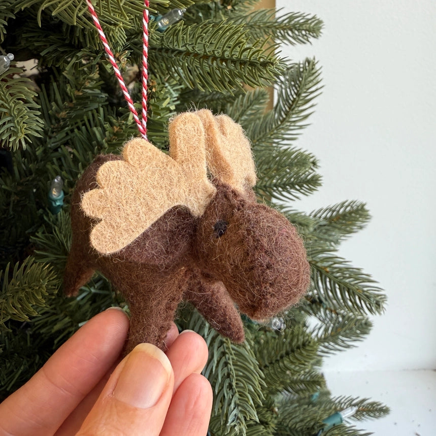 Moose-shaped ornament held in front of a Christmas tree