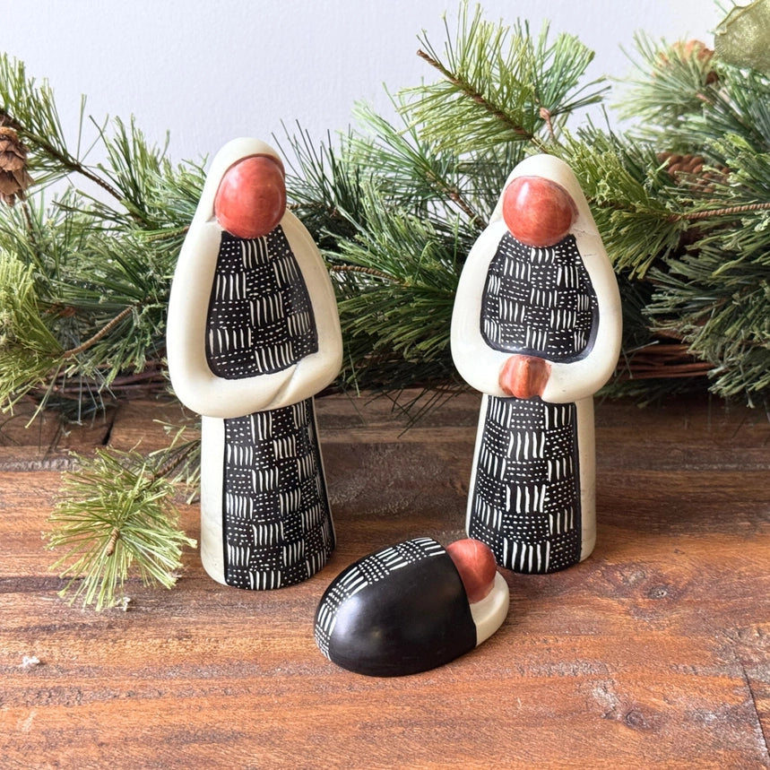 Mary and Joseph soapstone figures with baby Jesus in a black and white design on a wooden background.