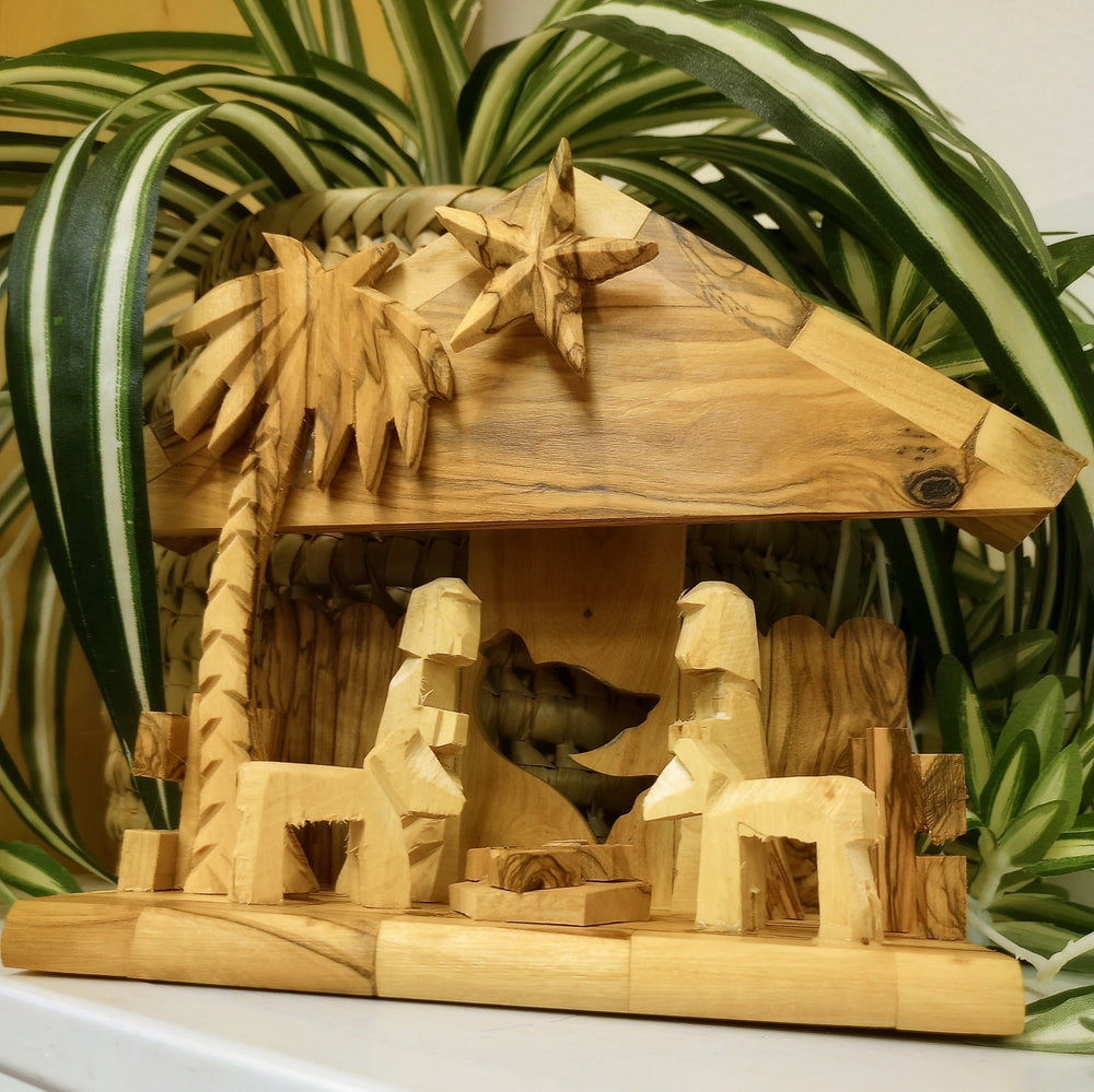 Wooden nativity scene with stable, palm tree, and animals with a plant in the background