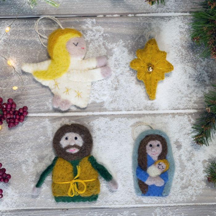Felt nativity scene ornaments on a wooden surface with Christmas decorations.
