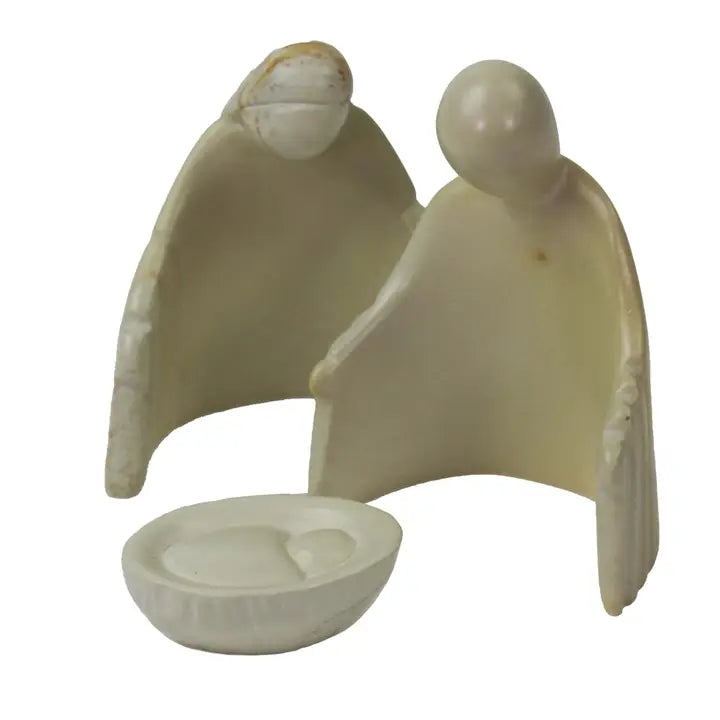 A small carved figurine depicting Mary and Joseph and a shallow basket with baby Jesus in front, made from a smooth off-white material soapstone, shown on a plain white background.