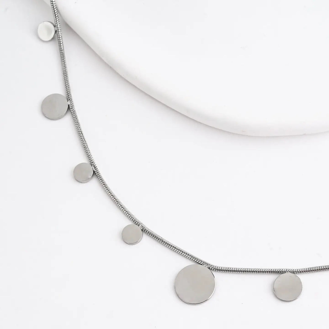 A silver necklace with silver disks on a white background. 