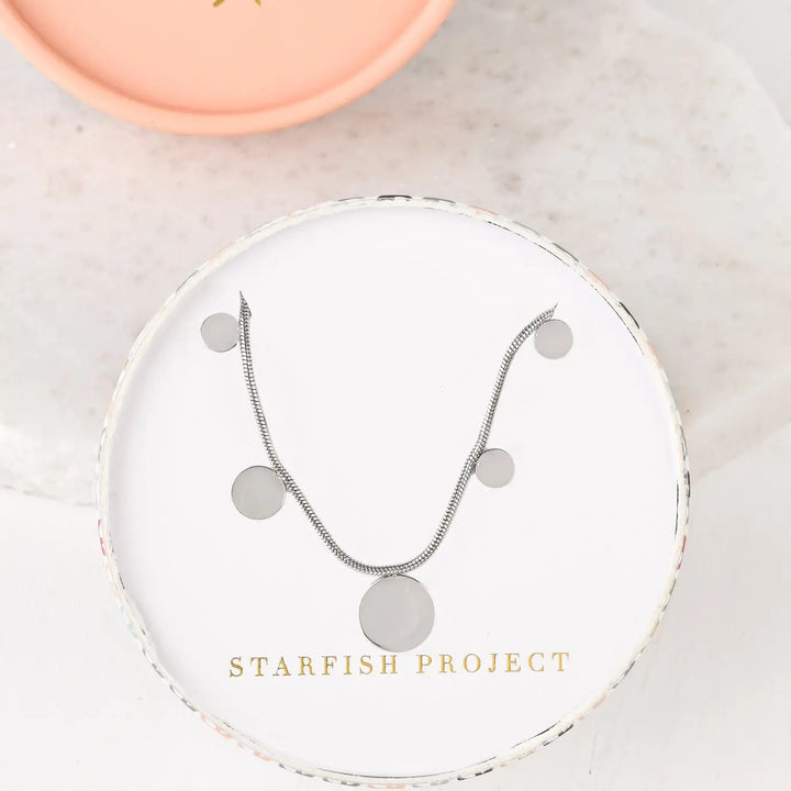 A silver necklace with silver disks in a Starfish Project gift box.
