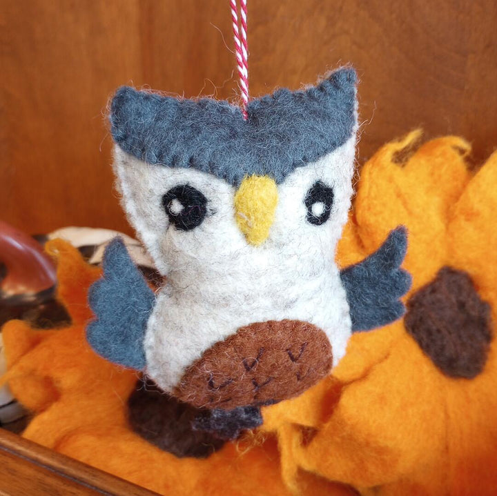 Felt owl ornament hanging among pumpkins on a wooden surface