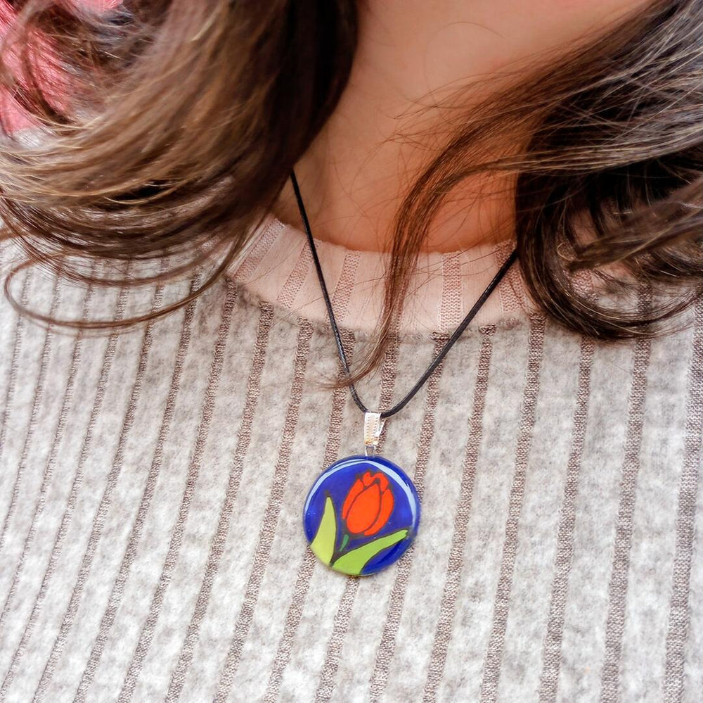 Necklace with a pendant featuring a tulip design worn by a person with striped clothing.