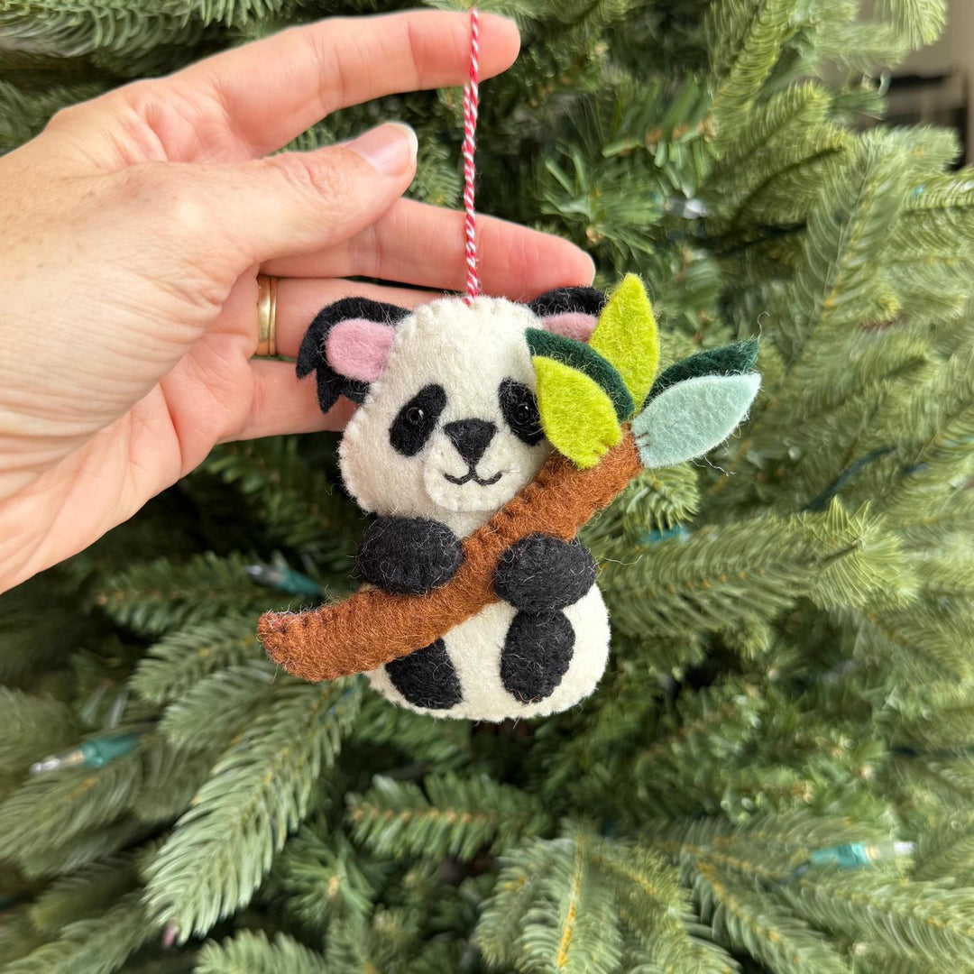 Hand holding a panda ornament with leaves against a Christmas tree background
